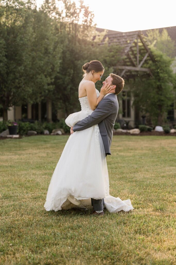 Leah and Joe share a romantic moment as he lifts her in RiverStone's garden during golden hour, with the pergola in the background.