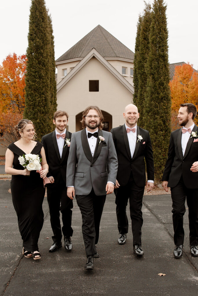 Nathan walks with his groomsmen along the pathway in front of RiverStone's stone-accented wedding venue.