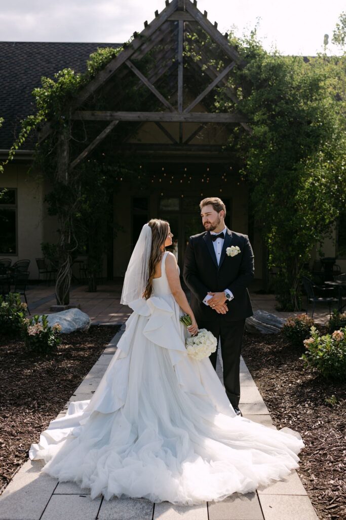 Sophie and Tyson stand together along a stone walkway in front of RiverStone's vine-covered wooden pergola.