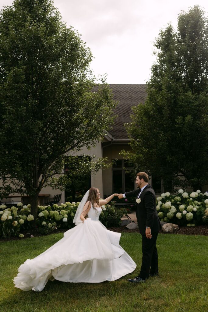 Sophie twirls in her flowing white wedding gown as Tyson holds her hand in RiverStone's green summer gardens.