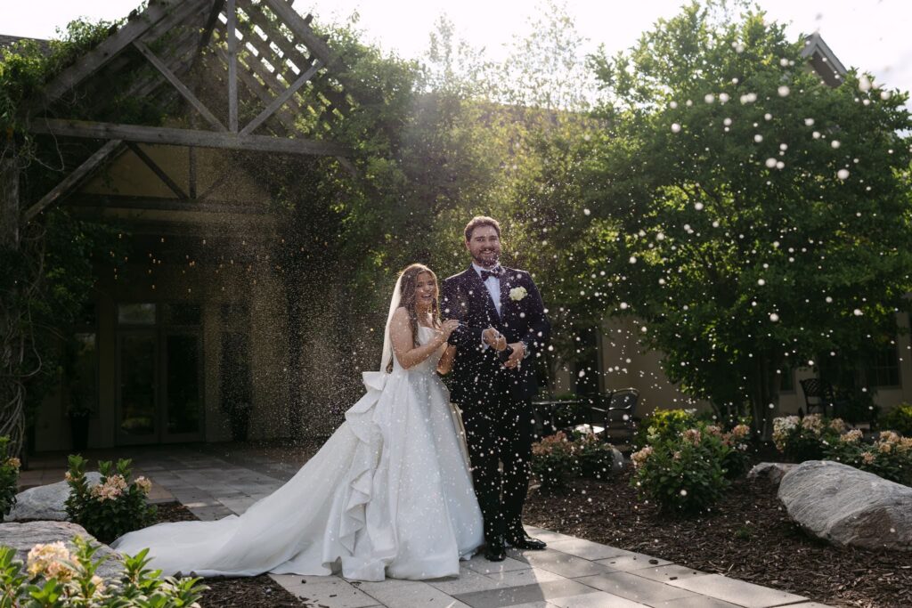 Sophie and Tyson celebrate with a spray of champagne in RiverStone's sunlit outdoor courtyard.